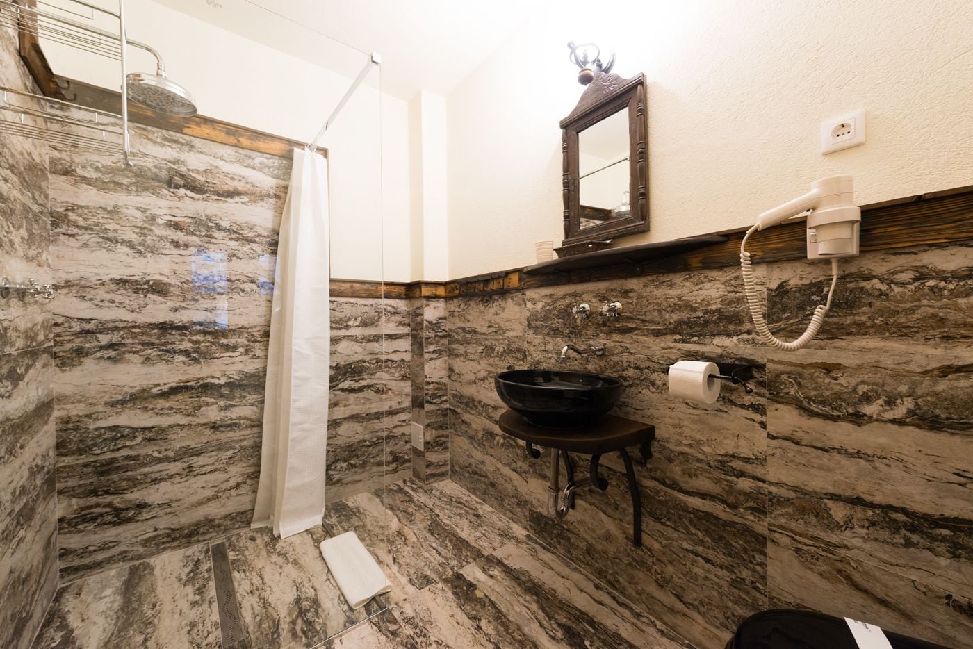 A bathroom with a marble floor, a black sink, a shower, and a mirror.