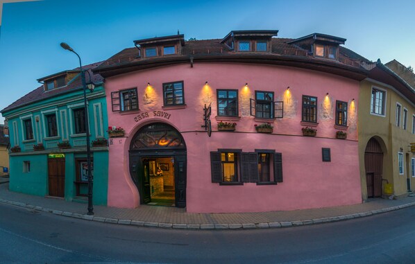 A pink building with a sign reading "ESSA SAVRI" and a green building adjacent to it. - Casa Savri (Sighisoara)