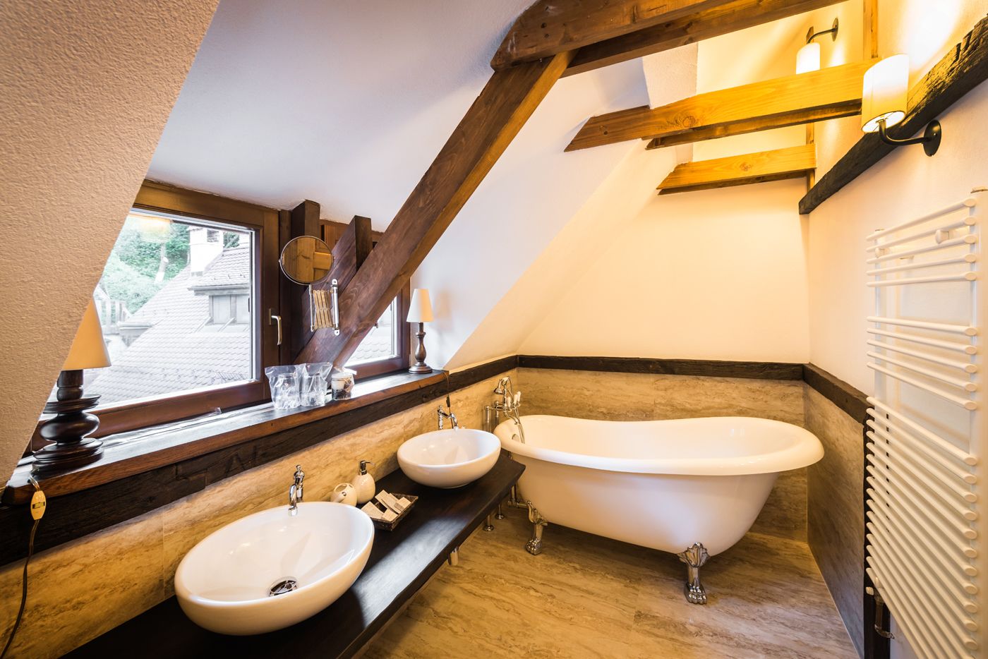 A bathroom with a large bathtub, two sinks, and a window with a view of a building outside.
