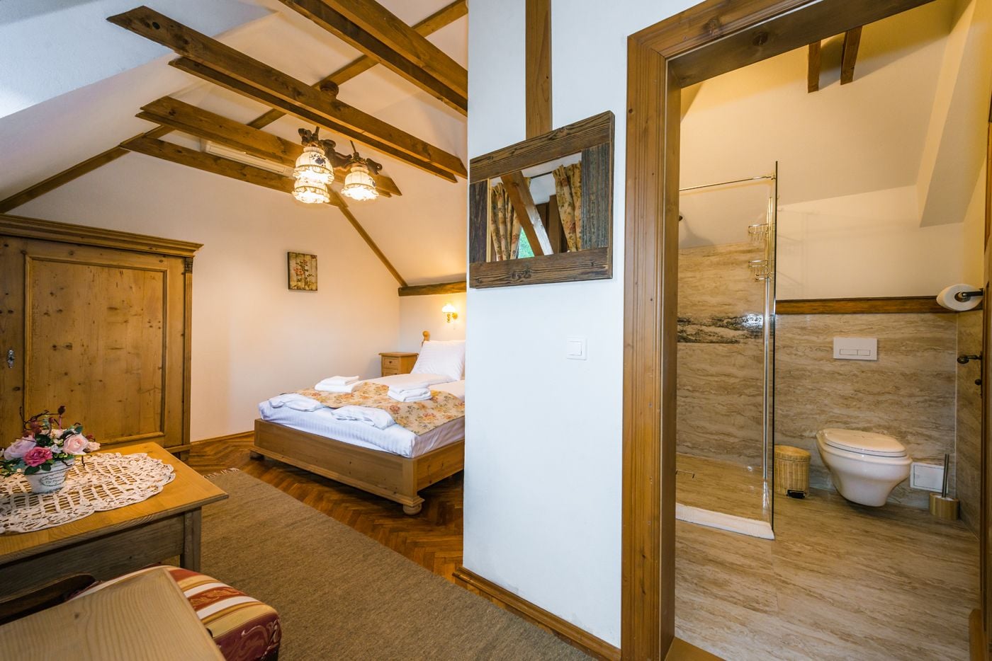 A bedroom with a wooden bed, a nightstand, and a dresser. There is a bathroom with a toilet, a shower, and a mirror.