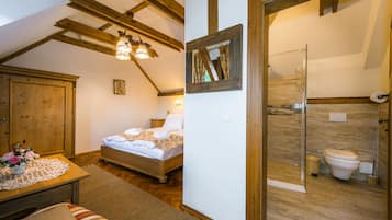 A bedroom with a wooden bed, a nightstand, and a dresser. There is a bathroom with a toilet, a shower, and a mirror.