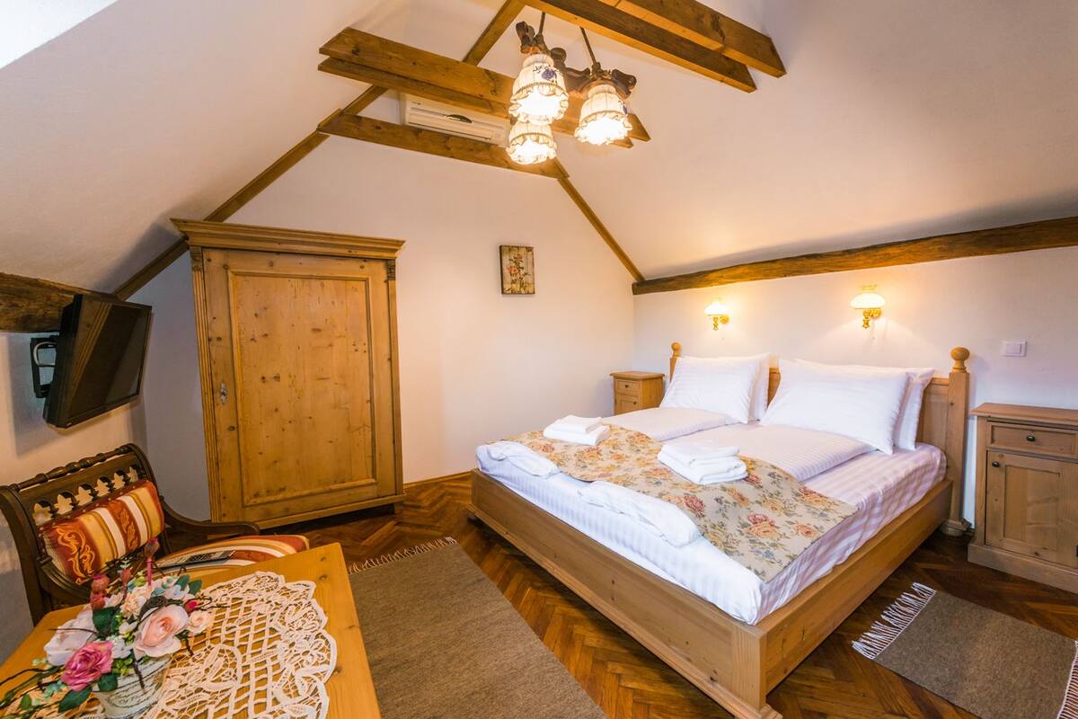 Un dormitorio con cama de madera, una mesita de noche, un armario de madera, un televisor en la pared y un ventilador de techo.