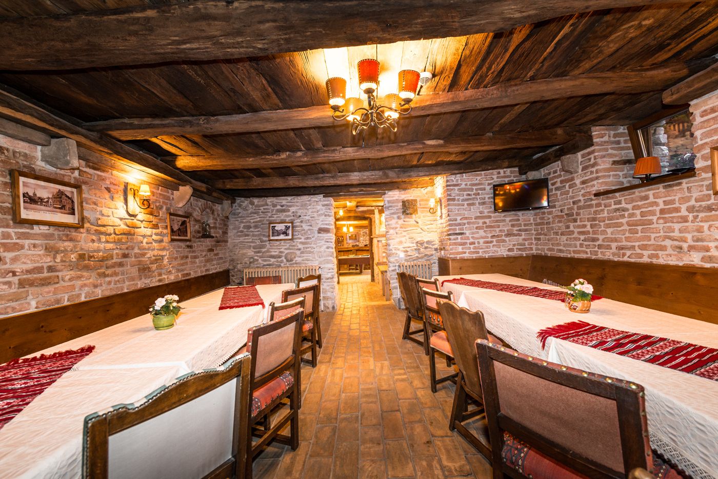 Un coin repas rustique avec des tables en bois, des murs en pierre et un lustre.