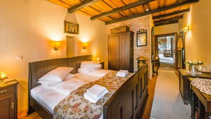 Habitación de hotel con techo de madera, una cama grande con ropa de cama floral, un armario de madera y una mesita con un jarrón de flores.