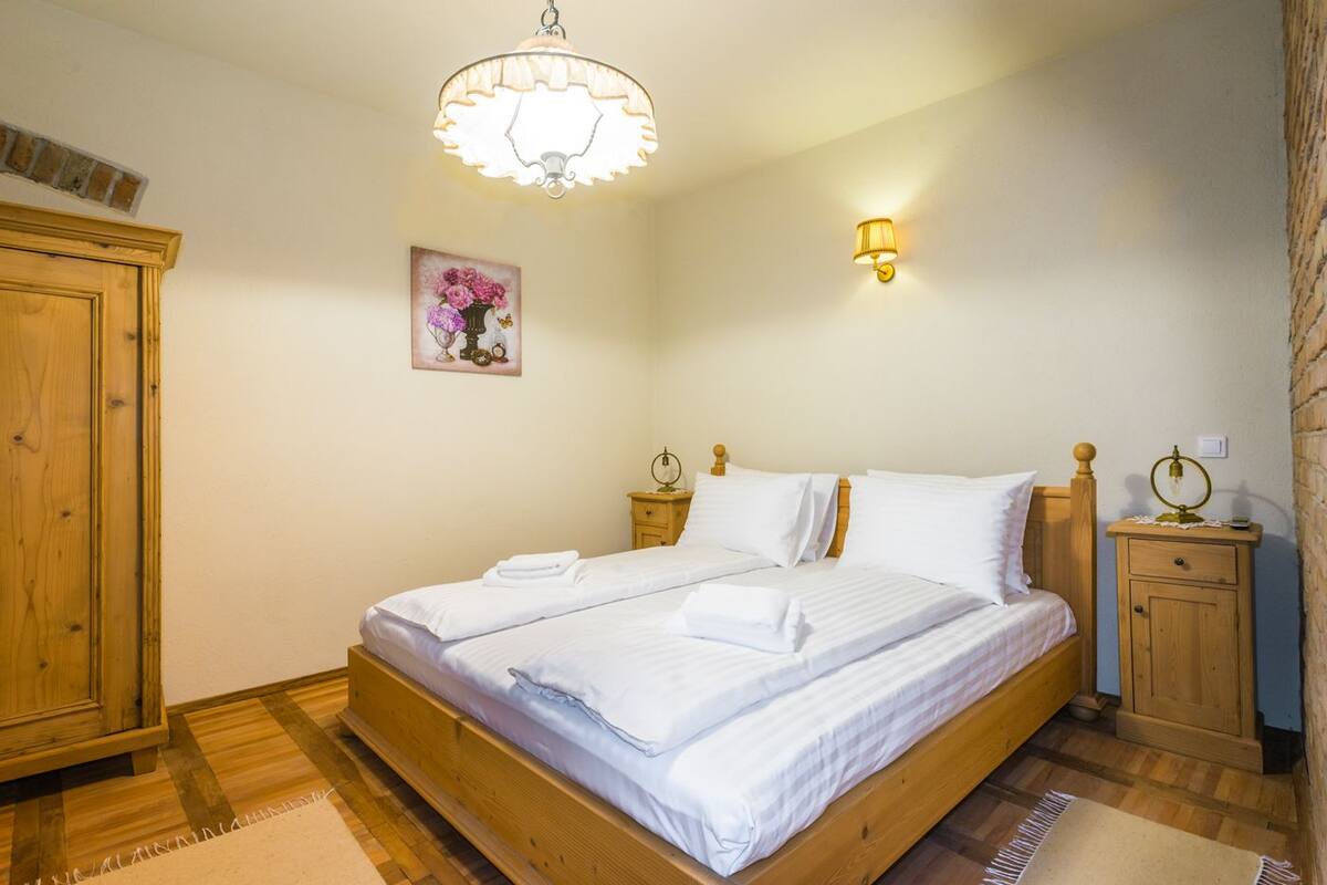 Un dormitorio con cama de madera, mesita de noche, lámpara de pared y una imagen de flores.