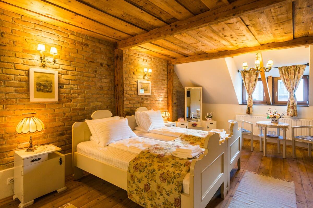 Un dormitorio acogedor con dos camas, vigas de madera, paredes de ladrillo y una zona de comedor con mesa y sillas.