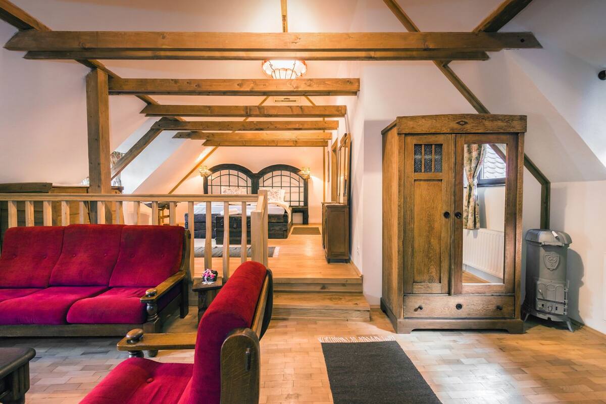 Un dormitorio tipo loft acogedor con techo de madera, un sofá rojo, una mesita pequeña y un armario de madera.