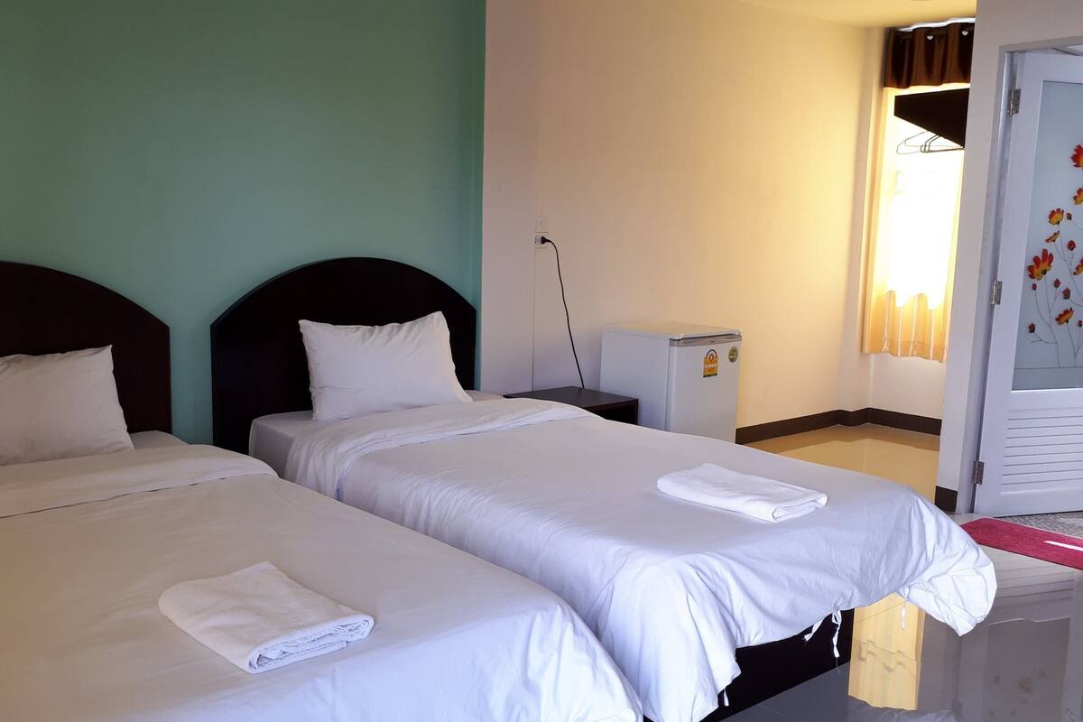 Una habitación de hotel con dos camas individuales, un refrigerador pequeño, un escritorio y una ventana con cortinas.