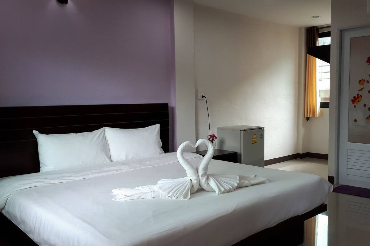 Una habitación de hotel con una cama bien hecha, un refrigerador pequeño y una puerta con diseño floral.