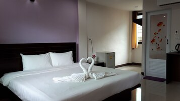 Quarto de hotel com cama bem arrumada, uma pequena geladeira e porta com desenho floral.