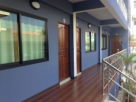Corredor com portas e janelas de madeira, corrimão de metal e chão de azulejos.