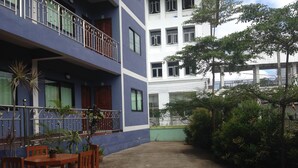 A courtyard with a wooden table and chairs, surrounded by potted plants and a blue building with balconies. - Nan Green View Hotel (Nan)