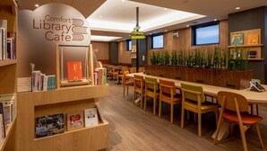 Um café em biblioteca, com estantes de livros, uma mesa comprida e cadeiras.