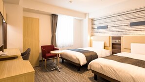 Quarto de hotel com duas camas, uma escrivaninha, uma cadeira e uma mesinha.