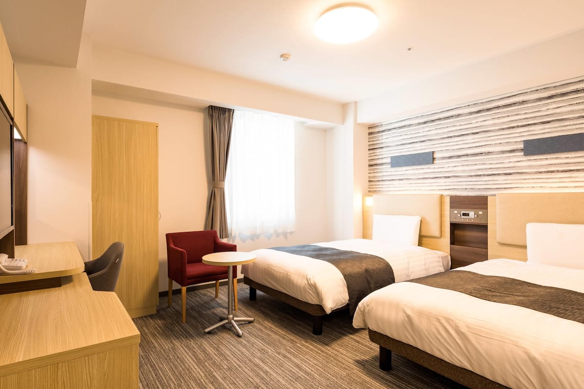 Une chambre d’hôtel avec deux lits, un bureau, une chaise et une petite table.