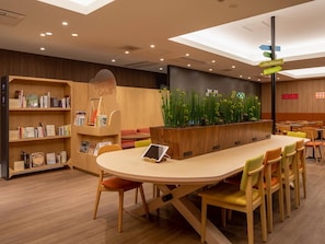 Un café moderne situé dans une bibliothèque, avec une longue table, des chaises, des étagères et un mur végétal décoratif.