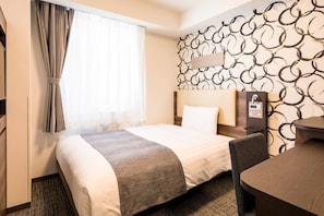 Hotelkamer met een bed, bureau, stoel, raam met gordijnen en een muur met een rond patroon.