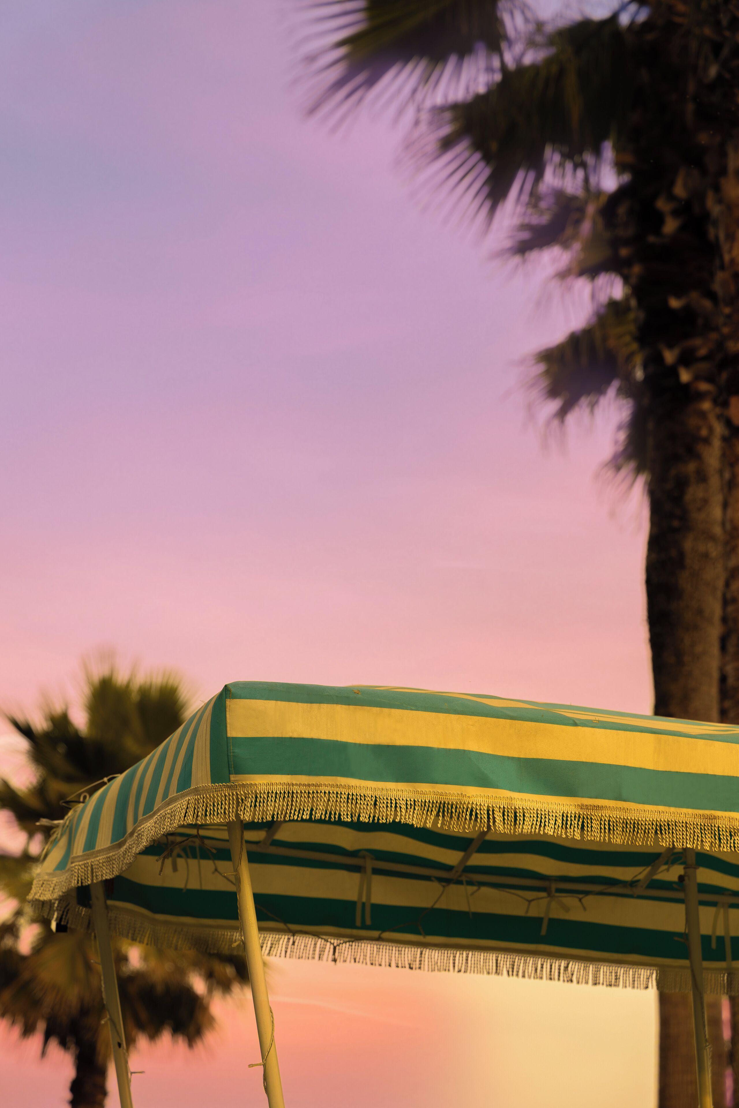 A beach umbrella with a striped pattern, set against a sunset sky.
