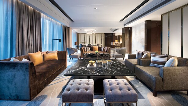Een moderne hotellobby met een centrale zithoek, een eettafel en een bar.