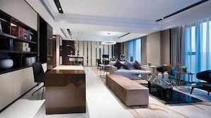 Een moderne hotelkamer met een houten receptiebalie, een bank, een eethoek en grote ramen met gordijnen.