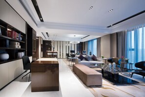 Une chambre d’hôtel moderne avec un comptoir d’accueil en bois, un canapé, un coin repas et de grandes fenêtres équipées de rideaux.