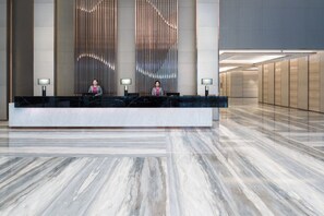 Un comptoir d’accueil d’hôtel avec deux employés, un design intérieur moderne et un sol en marbre.