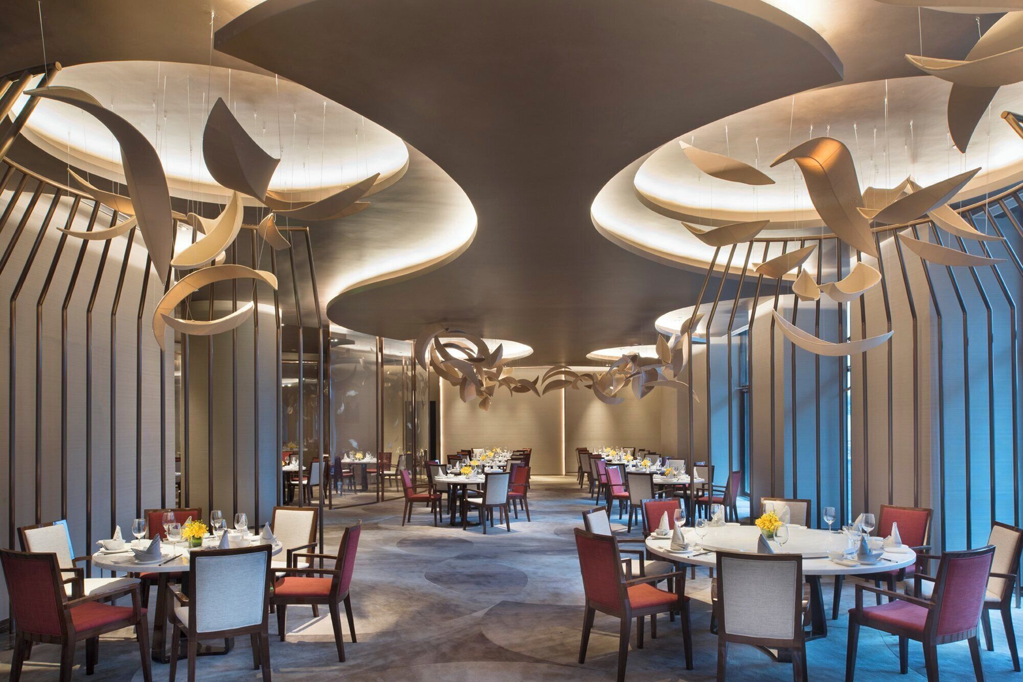 A modern dining area with round tables, chairs, and a unique ceiling design.