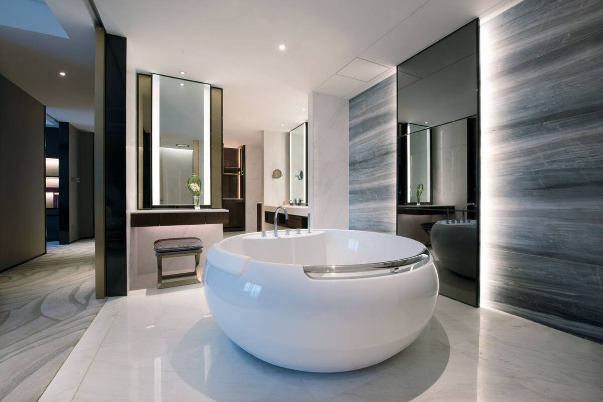 A modern bathroom with a large, round bathtub, a bench, and a large mirror.
