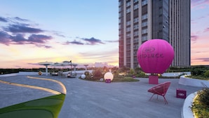 Ein moderner Außenbereich mit einem großen, rosafarbenen Ballon, Sitzgelegenheiten und einem hohen Gebäude im Hintergrund.