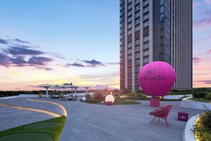 A modern outdoor area with a large pink balloon, seating, and a tall building in the background.