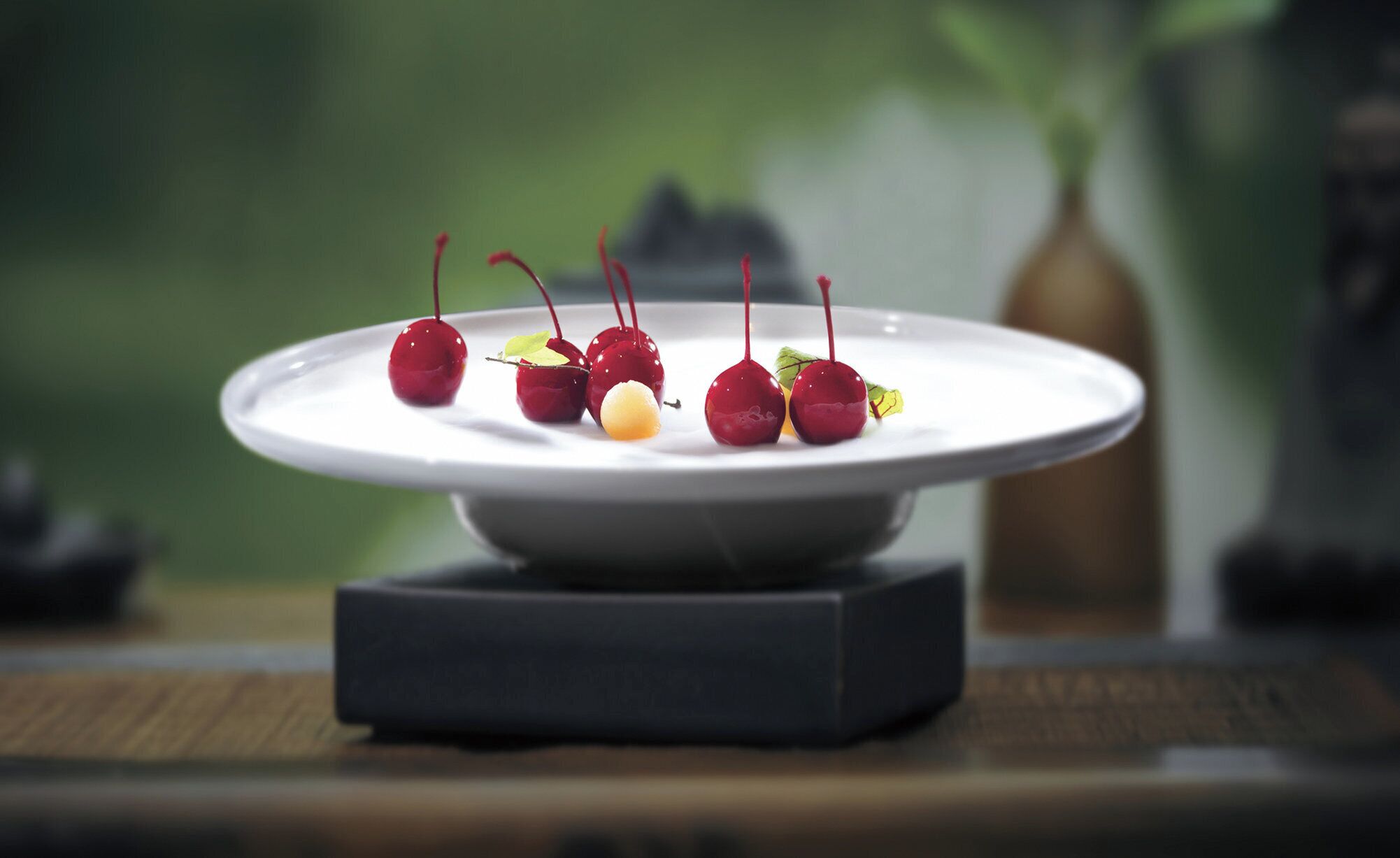 Une assiette blanche avec des cerises et un petit objet jaune posé sur un support foncé.
