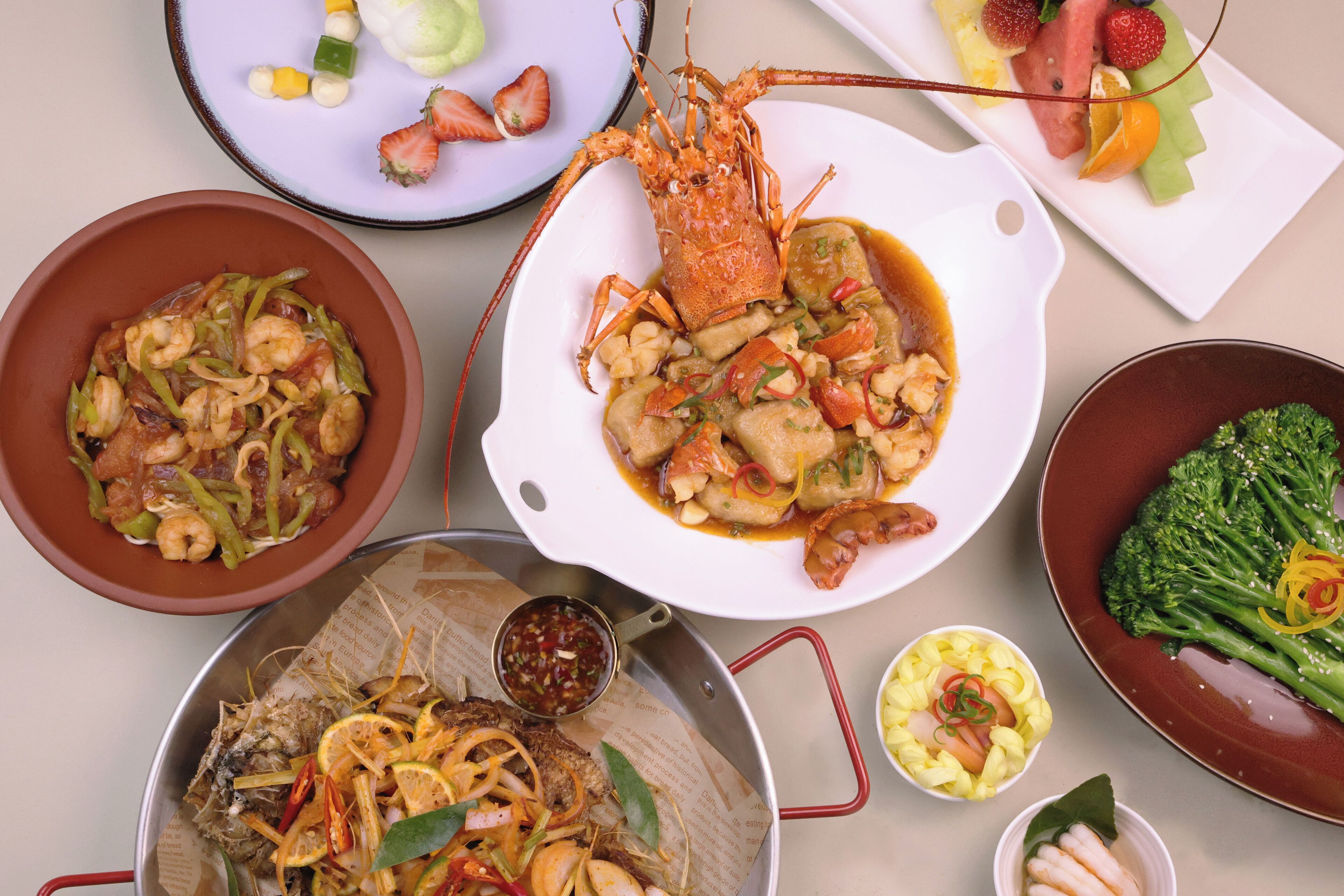 A variety of dishes including seafood, vegetables, and a lobster, served on multiple plates and bowls.