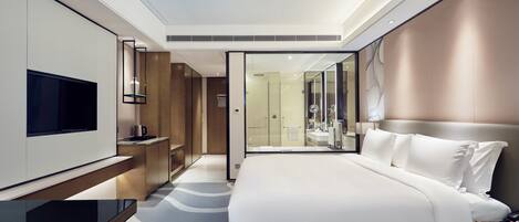 A modern hotel room with a large bed, a flat-screen TV, a desk, and a walk-in closet.