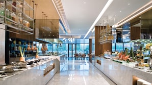 Een moderne hotel lobby met een marmeren vloer, glazen scheidingswanden en een buffet met diverse gerechten.