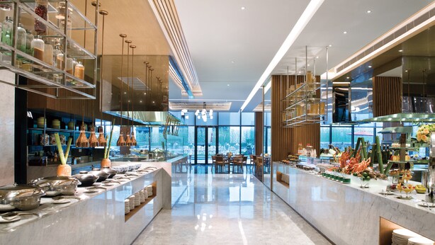 Eine moderne Hotelhalle mit Marmorboden, Glastrennwänden und einem Buffetbereich mit verschiedenen Speisen.