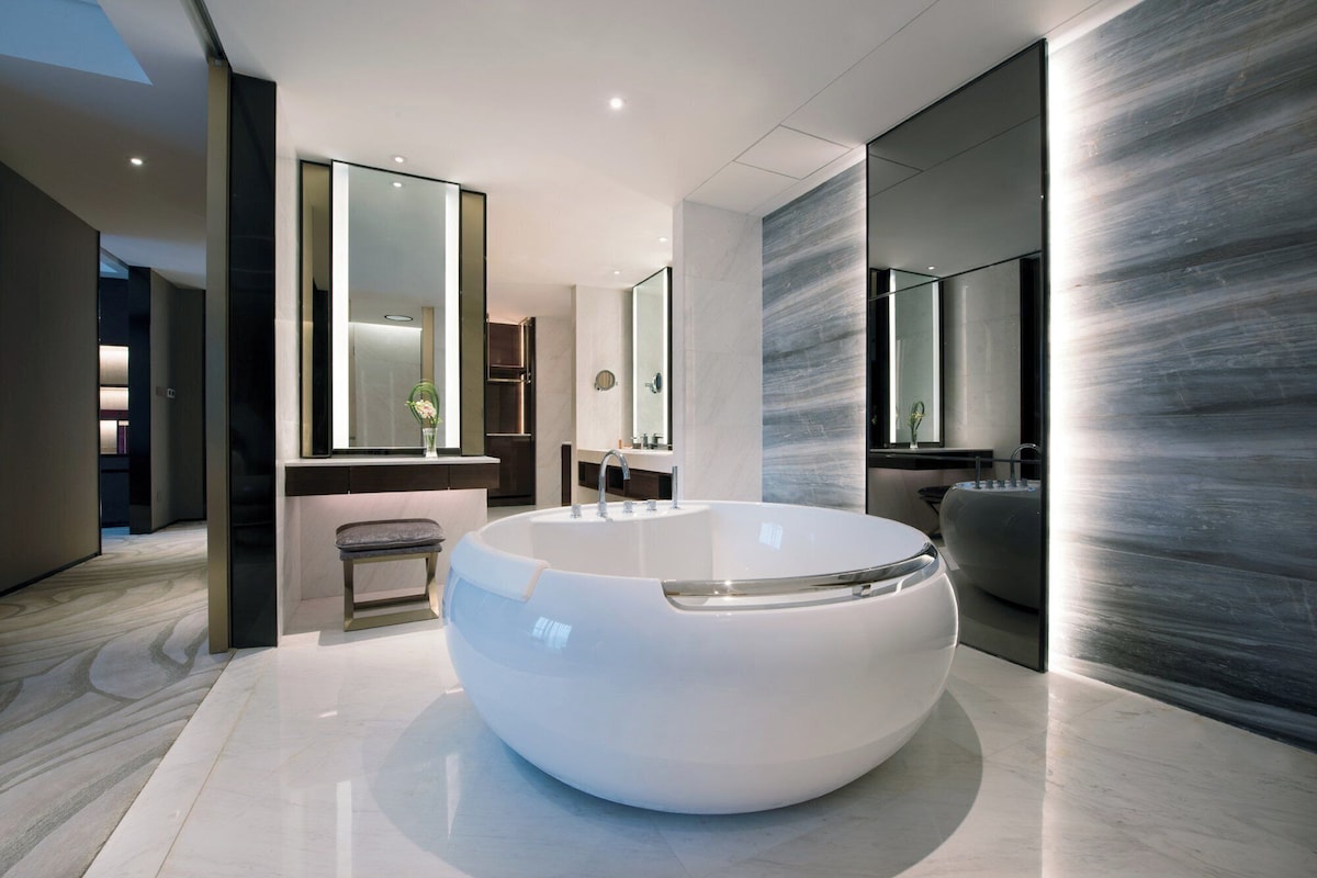 A modern bathroom with a large, round bathtub, a mirror, and a sleek, minimalist design.