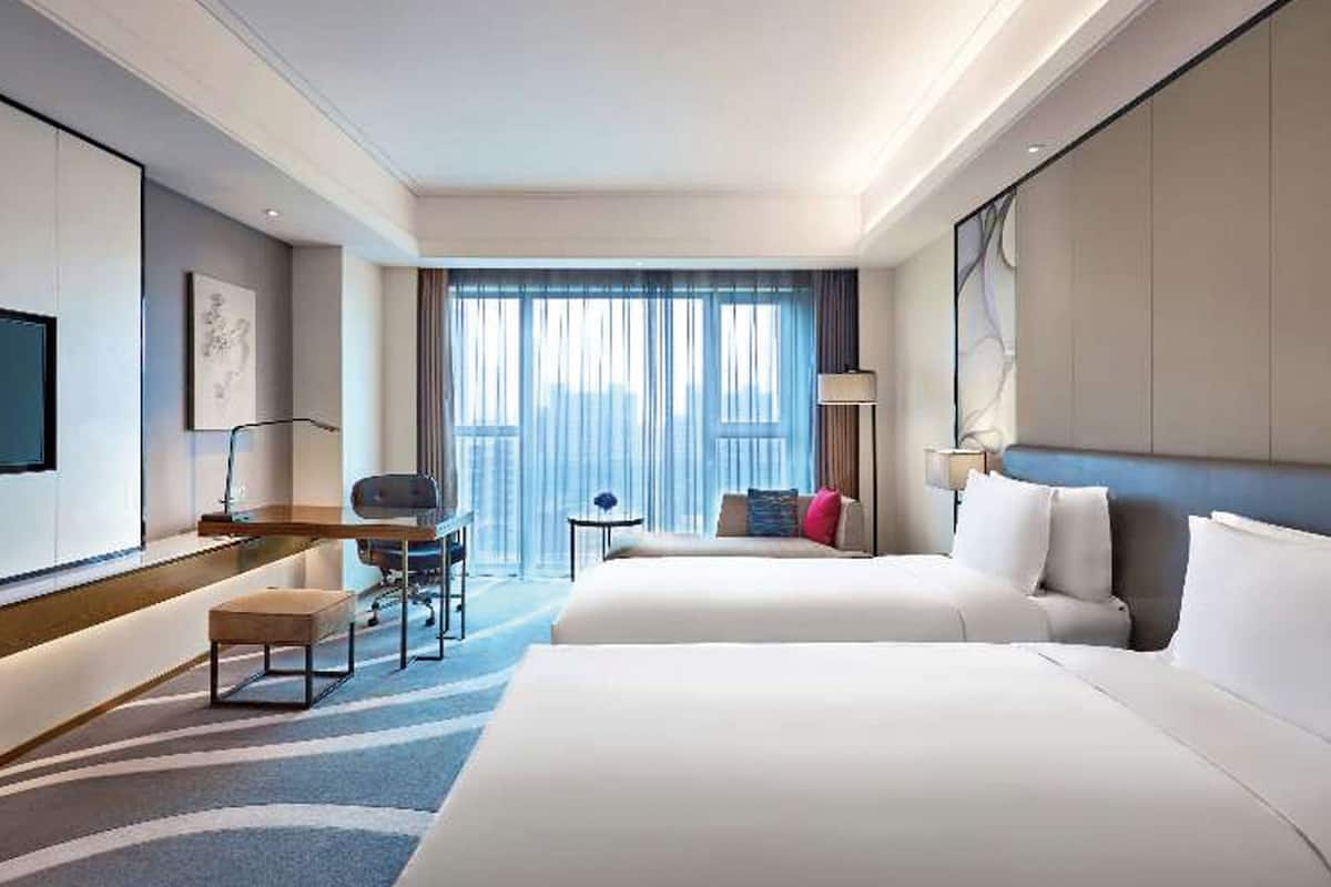 A hotel room with two beds, a desk, a chair, a small table, and a TV.