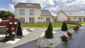 Une maison à deux étages, avec un toit en tuiles, une pelouse devant et des plantes en pot.
