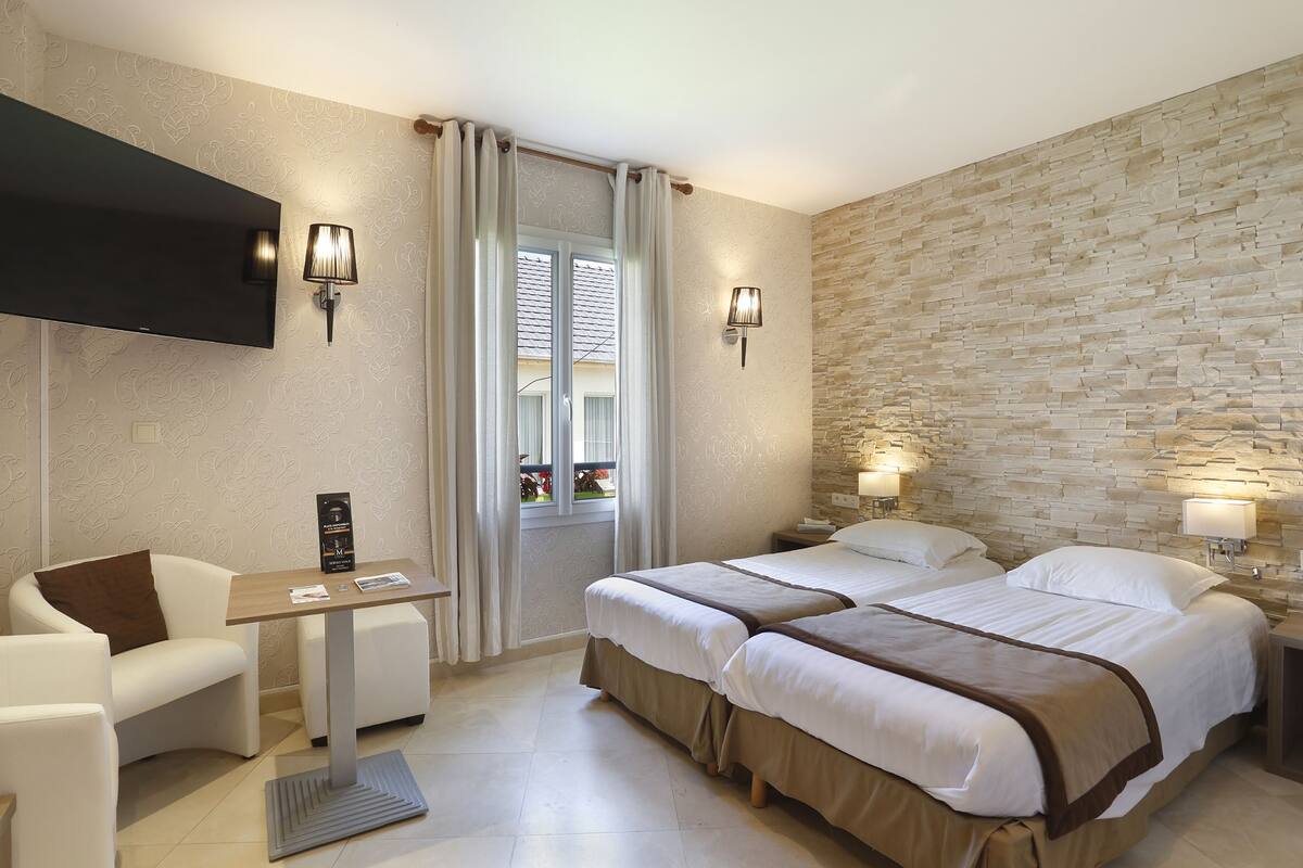 Habitación de hotel con dos camas, un escritorio, una silla y un televisor.