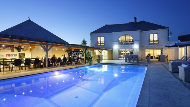 Une piscine dotée d’une zone couverte et un bâtiment avec un balcon.