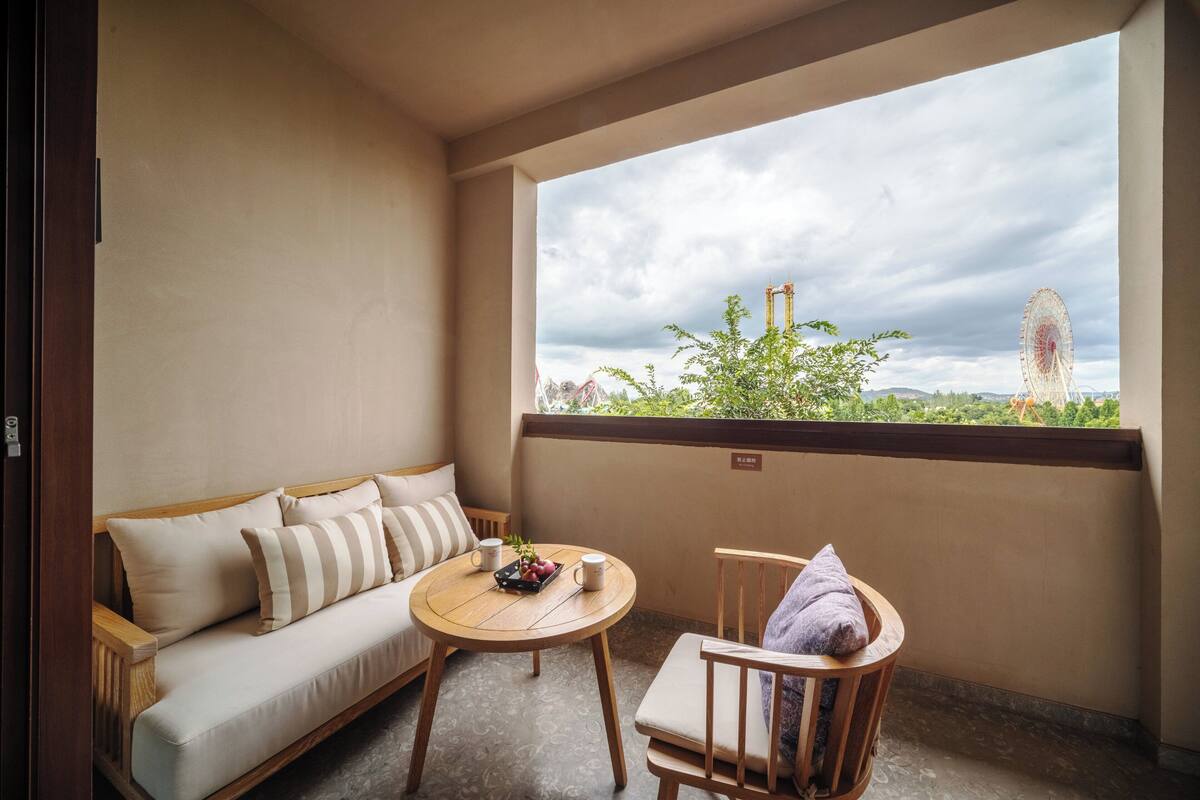 Un balcon avec un canapé, une petite table sur laquelle se trouve un plateau de fruits et deux tasses, et une chaise avec une serviette.
