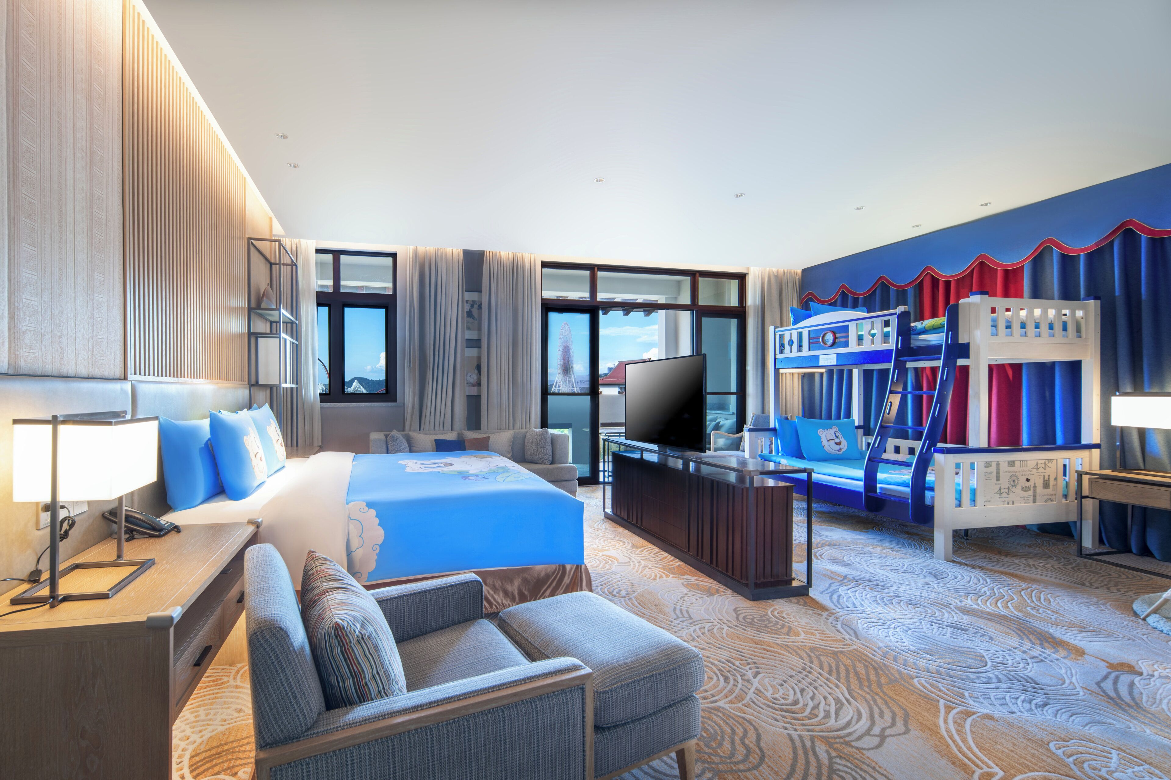 A hotel room with a large bed, a desk with a lamp, a sofa, a TV, and bunk beds.