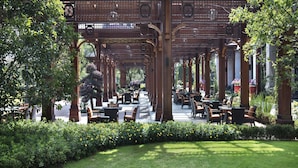 Un café en plein air doté de pergolas, de tables et de chaises en bois, entouré de verdure et de fleurs.