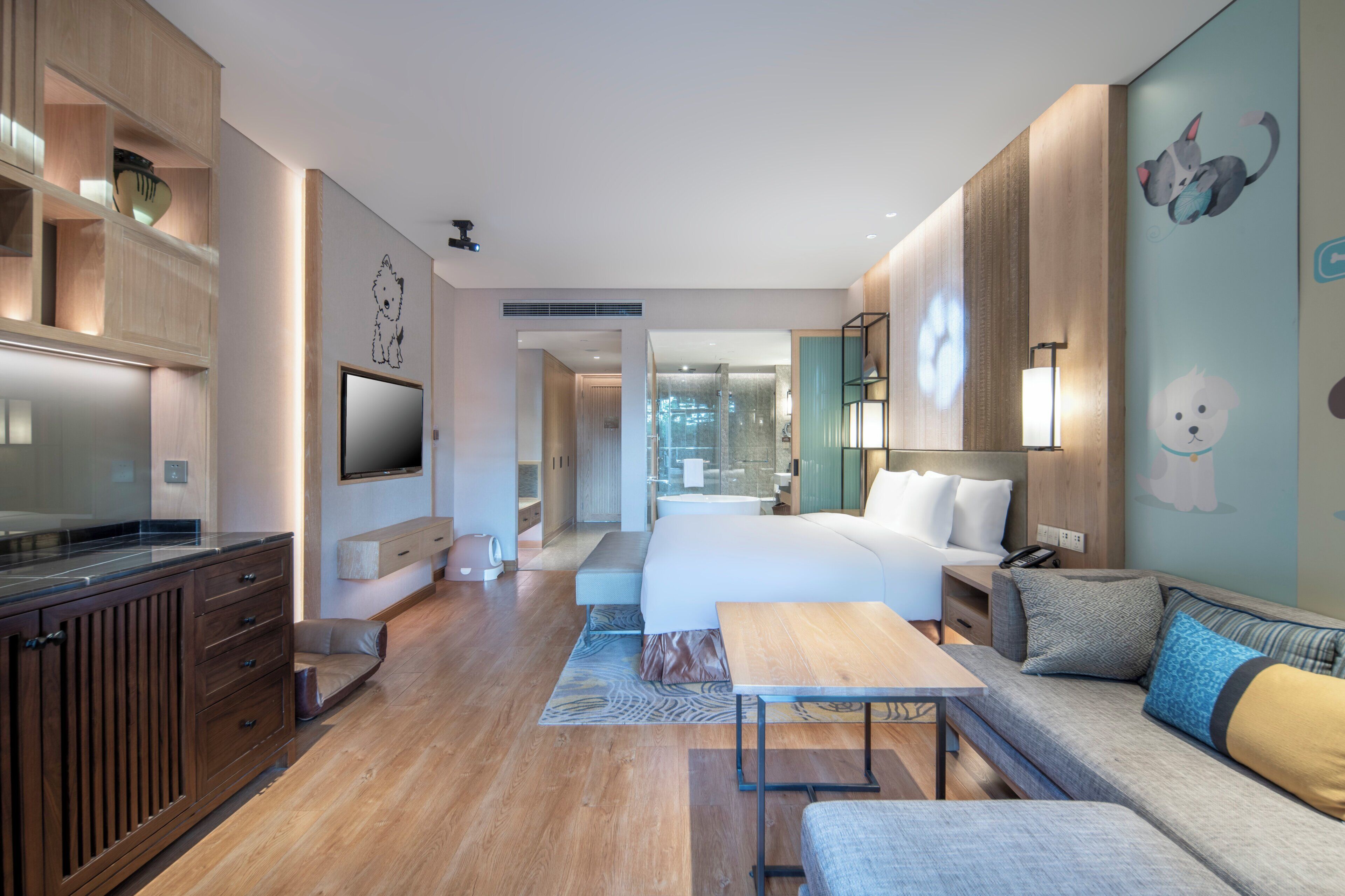 A modern hotel room with a wooden floor, a large bed, a sofa, a desk, and a TV.