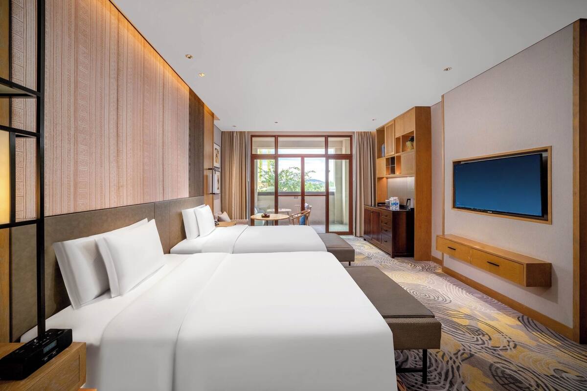 Une chambre d’hôtel avec deux lits, une télévision, un bureau et une vue sur l’extérieur.