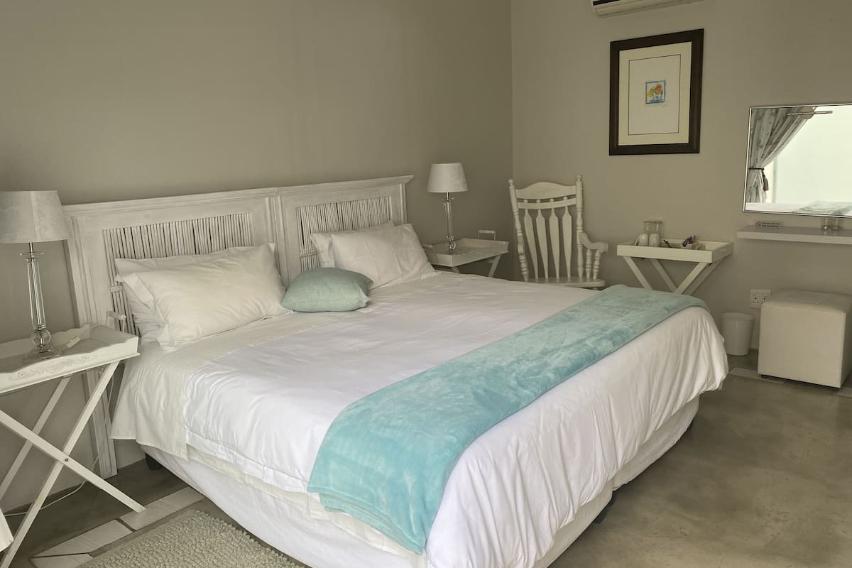 Une chambre bien rangée, avec un grand lit, des tables de chevet, une chaise, un bureau et un appareil de climatisation.