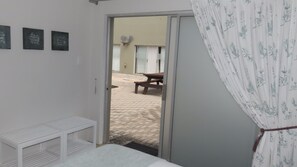 Una habitación con cama, un banco y una puerta que da a un espacio exterior con una mesa de picnic y un edificio al fondo.