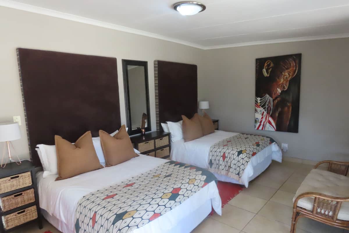 Une chambre d’hôtel avec deux lits, un grand miroir, un tableau accroché au mur, une chaise et un tapis rouge.