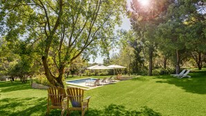 Ein Garten mit Schwimmbad, Liegestühlen und einem Baum.