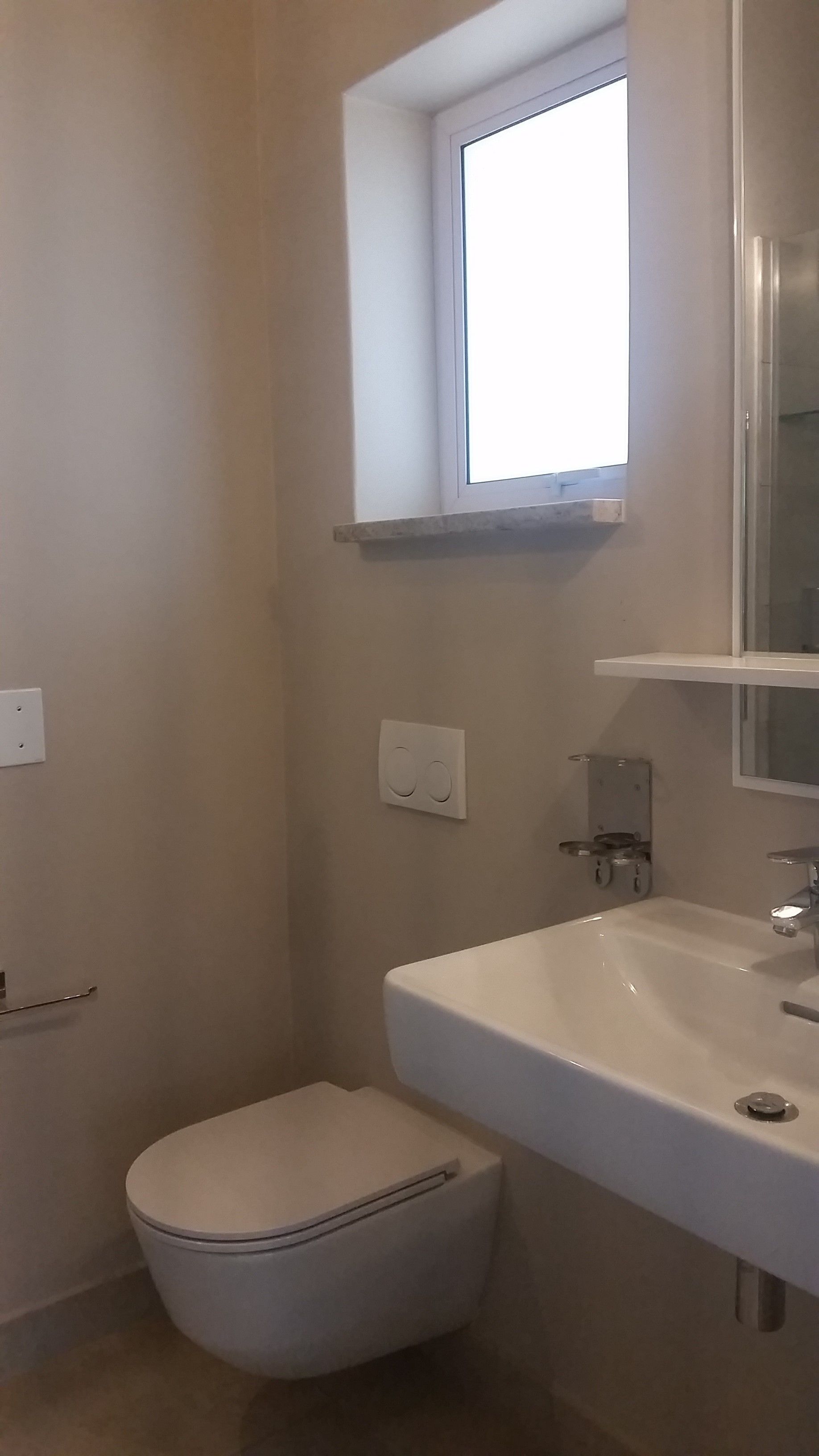 A small, clean bathroom with a toilet, sink, and a window above the mirror.